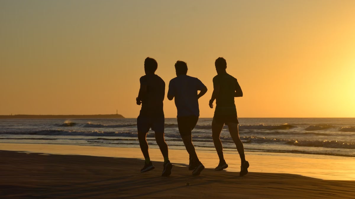 Three people running at sunset on Necochea Beach, Buenos Aires, creating striking silhouettes against the ocean waves.