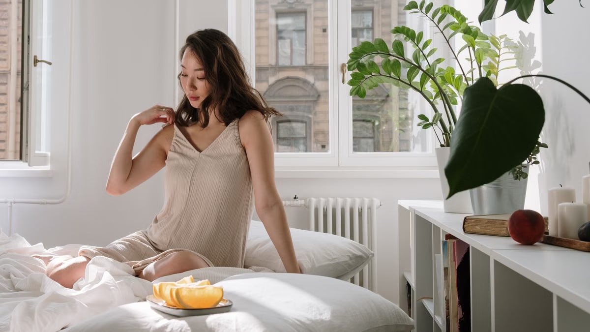 Asian woman in a cozy bedroom enjoying a calm morning with fresh citrus slices on a bed.